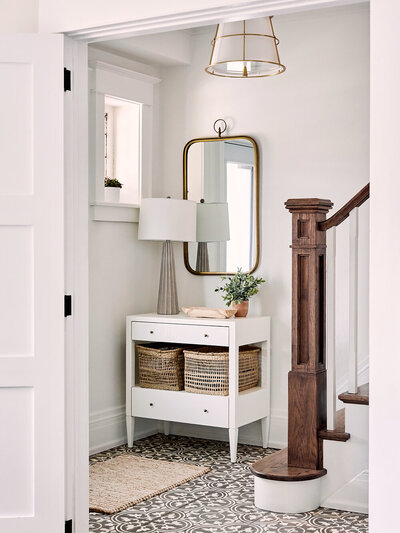 coastal inspired entry with patterned tile floors white walls wood newel post gold mirror and accents